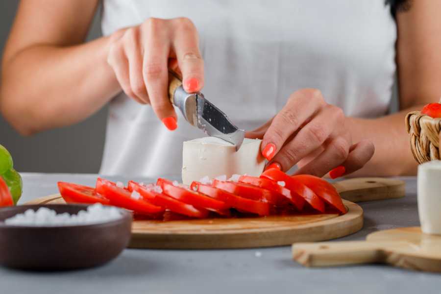 woman-slicing-cheese-cutting-board-with-sliced-tomatoes-salt-gray-surface-1.jpg